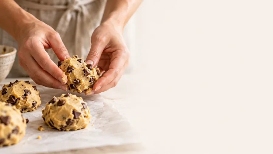 Hands gently shaping chocolate chip cookie dough on parchment